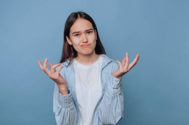 Stüdyoda hareketli, kafası karışmış genç bir kadın açık mavi arka planda belirsizlik ve merak duygularını vurguluyor.