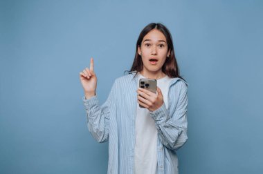 Açık mavi arka planda akıllı telefonu tutan genç bir kadının portresi