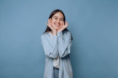 Genç kadın neşeli pozlar veriyor, canlı kişiliğini açık mavi arka planda parlak bir gülümsemeyle sergiliyor.