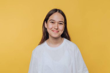 Parlak bir gülümseme, genç bir kadının parlak sarı arka planda gelişigüzel poz vermesinden yayılıyor.