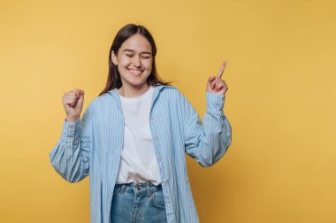 Neşeli kadın heyecanla dans ediyor, mutluluğu canlı sarı arka planda ifade ediyor.