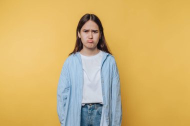 Kadın ciddi bir ifade sergiliyor. Vücut dili, canlı sarı arka planda derin duygular taşıyor.