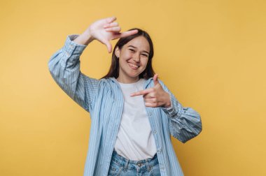 Genç bir kadın, canlı sarı arka planda yaratıcılık ve hayal gücüyle dolu bir sahneyi şakayla çerçeveliyor.