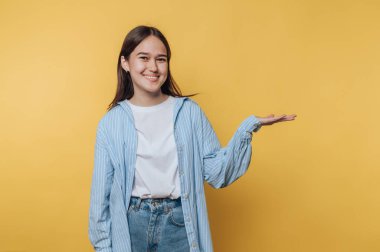 Genç bir kadın, parlak sarı arka planda dostça bir jest yaparak elini uzatıyor.