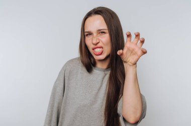 Oyuncu kadın pençeli bir el hareketiyle vahşi bir bakışı taklit ediyor, beyaz arka plandaki yüz ifadesindeki mizahı vurguluyor.