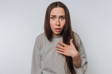 Şok olmuş, uzun saçlı genç bir kadın şaşkınlık ve şaşkınlık içinde. Beklenmedik bir duruma duygusal bir tepki gösteriyor. Ya da beyaz arka plandaki haberlere.