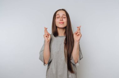 Umut dolu bir ifadeye sahip genç bir kadın umut dolu parmaklarını çapraz yapar, iyimserliğin özünü ve beyaz arka planda iyilik arzusunu somutlaştırır.