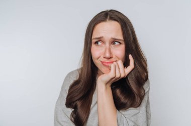 Genç bir kadın endişeli bir ifade sergiliyor, içsel düşüncelerini ve altta yatan kaygı ve endişelerini beyaz arka planda açıkça ifade ediyor.