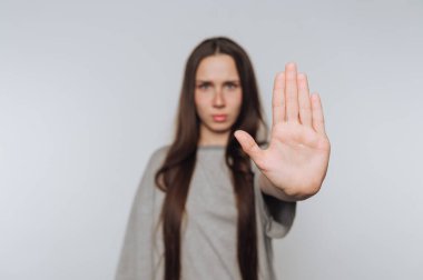 Kadın, beyaz arka plandaki etkileşimlerde sınırların ve kişisel alanın önemini simgeleyen bir duruş hareketi yaparak elini kaldırır.