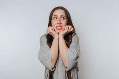 Genç bir kadın beyaz arka planda vücut dili ile korkusunu ifade eder.