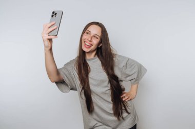 Oyuncu kadın akıllı telefonuyla neşeli bir anı paylaşmaktan hoşlanır, beyaz arka planda selfie çekmekten.