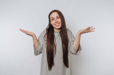 Uzun saçlı genç kadın neşeli bir ifade sergiliyor ve kollarını kaldırıyor. Beyaz arka planda neşe ve coşkuyu simgeliyor.