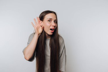 Genç bir kadın, beyaz arka plandaki konuşmada merak ve aktif bağlılık temasını göstererek dikkatle dinlerken şaşırmış görünüyor.