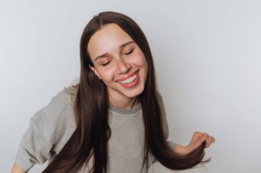 Uzun saçlı neşeli bir kadın mutluluğun tadını çıkarırken ışıl ışıl gülümser, beyaz arka planda neşe ve pozitiflik taşır.