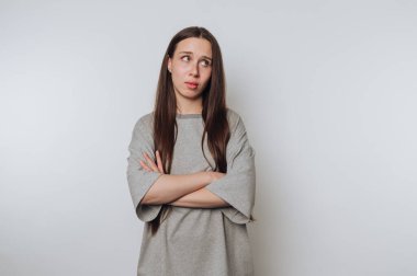 Düşünceli bir kadın kollarını kavuşturmuş, derin düşüncelere dalmış, beyaz arka planda derin duygusal düşünceleri yansıtıyor.