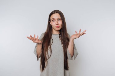 Şaşırmış bir kadın, beyaz arka planda belirsiz bir ifadeyle omuzlarını silker.