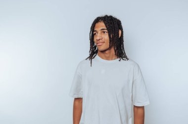 Beyaz tişörtlü genç adam beyaz arka planda duran dostça bir gülümseme sergiliyor.