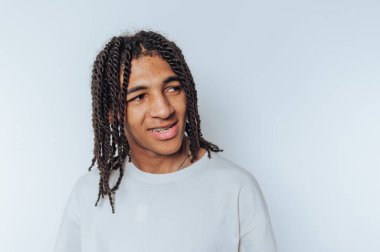 Beyaz gömlekli genç adam hafifçe yana dönüyor, beyaz arka planda gerçek bir gülümseme takınıyor.