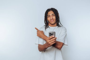 Genç adam, elinde akıllı bir telefon tutarken özgüvenle dikiliyor, bir an yön ve niyetini beyaz arka plana yansıtıyor.