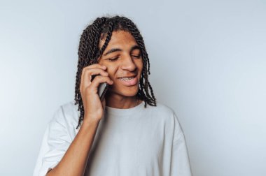 Genç adam akıllı telefonuyla konuşurken, beyaz arka planda bir bağlantı ve iletişim anını tasvir ederken sıcak bir şekilde gülümsüyor.