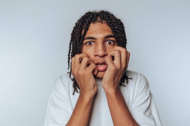 Genç insan korkmuş bir yüz ifadesi sergiliyor, elleri beyaz arka planda yüzünü tutuyor.