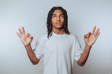 Genç insan dik dik bakıyor ve el hareketleriyle beyaz arka planda sükunet ve farkındalığı somutlaştırıyor.