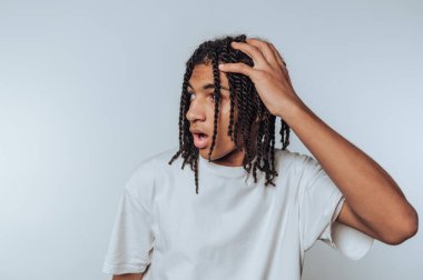 Genç adam, elini saçının arasında gezdirirken şaşkınlığını ifade ediyor. Beyaz arka planda bir an fark ediş ve yansıma olduğunu gösteriyor.