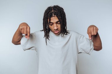 Genç bireyler tarafsız bir ifadeyle beyaz arkaplanı işaret ederek ayakta duruyorlar.