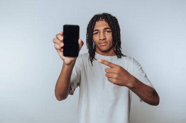 Kendine güveni tam bir genç, beyaz arka planda bir gülümsemeyle akıllı bir telefon tutuyor.