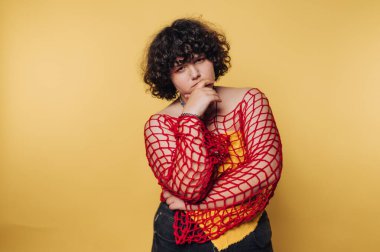 Kendine güvenen genç bir kadın, sarı arka planda canlı ve sanatsal bir kıyafet sergiliyor.