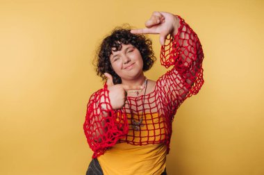 Geniş parmakları olan genç bir kadın sarı arka planda eğlenceli ve enerjik bir tavır sergiliyor.