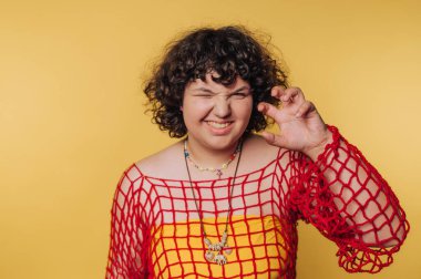 Genç bir kadın, sarı arka planda neşeli bir ifadeyle neşeli bir pençe hareketi sergiliyor.