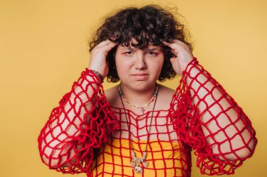 Genç bir kadın, sarı bir arka plana karşı renkli bir kıyafetle hayal kırıklığını ifade ediyor.