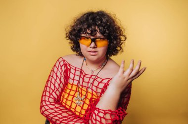 Güneş gözlüğü ve net bir bluz takan şık bir insan, sarı arka planda kendine güven ve modayı yansıtıyor.