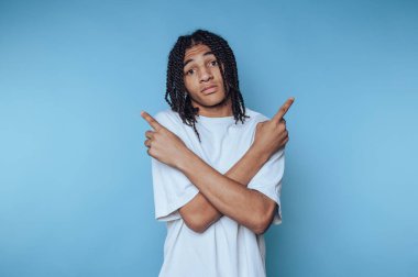 Genç adam farklı yönlere işaret ederken jestler yapar. Mavi arka planda kararsızlık hissi yaratır.