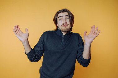 Genç bir adam sıradan bir anda saf sarı bir arka plana karşı belirsizlik gösteriyor.