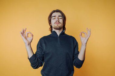 Genç adam parlak sarı bir arkaplan önünde meditasyon yapıyor.