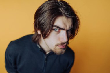 Uzun saçlı, turuncu arka planda meraklı bir genç adam. Kapalı mekandaki sıradan bir an sırasında.