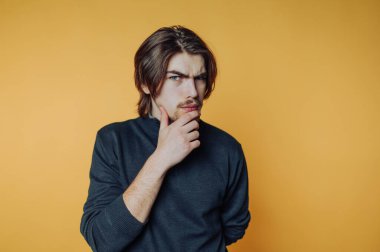 Genç adam, bir stüdyo oturumu sırasında parlak sarı bir zemin üzerinde düşünceli bir şekilde kafa yoruyor.