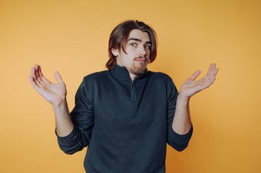 Canlı turuncu bir geçmişe karşı sıradan bir ifadeye sahip genç adam omuz silkerek belirsizlik gösteriyor.