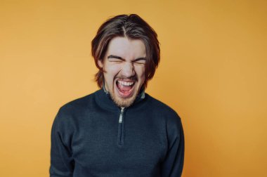 Heyecanlı genç bir adam parlak turuncu bir arka plana gülümsüyor. Canlı duygular sergiliyor.