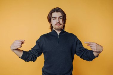 Kendine güveni olan genç bir adam, sıradan bir ev ortamında parlak sarı bir arkaplanı işaret ediyor.