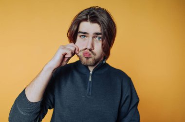 Genç adam neşeli bir şekilde poz verirken canlı turuncu arka plana karşı komik bir yüz ifadesi takınıyor.