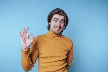 Rahat balıkçı yaka kazaklı genç bir adam parlak mavi bir arka plana 