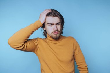 Genç adam açık mavi bir arkaplanda iç etkinlik sırasında durarak kafa karışıklığını ifade ediyor