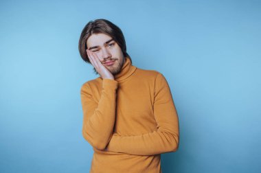 Sarı kazaklı genç adam mavi arka planda düşünceli bir şekilde poz veriyor, bir anlık içgözlem ve tefekkür görüntüsü yakalıyor.