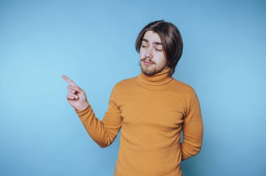 Genç bir adam, parlak bir stüdyoda mavi bir arka plana karşı güvenle el kol hareketi yapıyor.