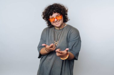 Turuncu güneş gözlüklü, gri bir tişörtle neşeli poz veren, neşeli ve neşeli bir kişilik sergileyen kişi.