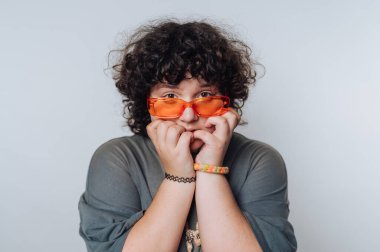 Bir insanın yüzüne yansıyan endişe ifadesi, renkli güneş gözlükleri ve tarafsız bir ortamda neşeli davranışlar sergiliyor.