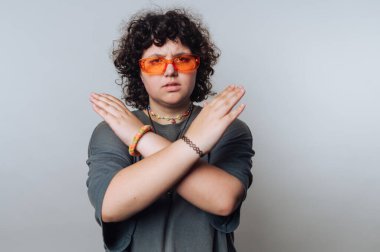 Genç kişi turuncu güneş gözlüğü ve stüdyo ortamında ciddi bir ifadeyle poz veriyor.